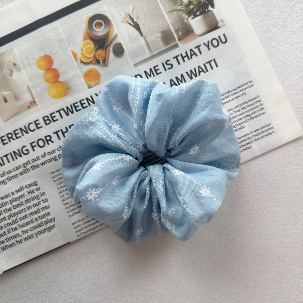 Close-up of white daisy embroidery on sky blue cotton scrunchie, high-quality artisanal hair accessory.