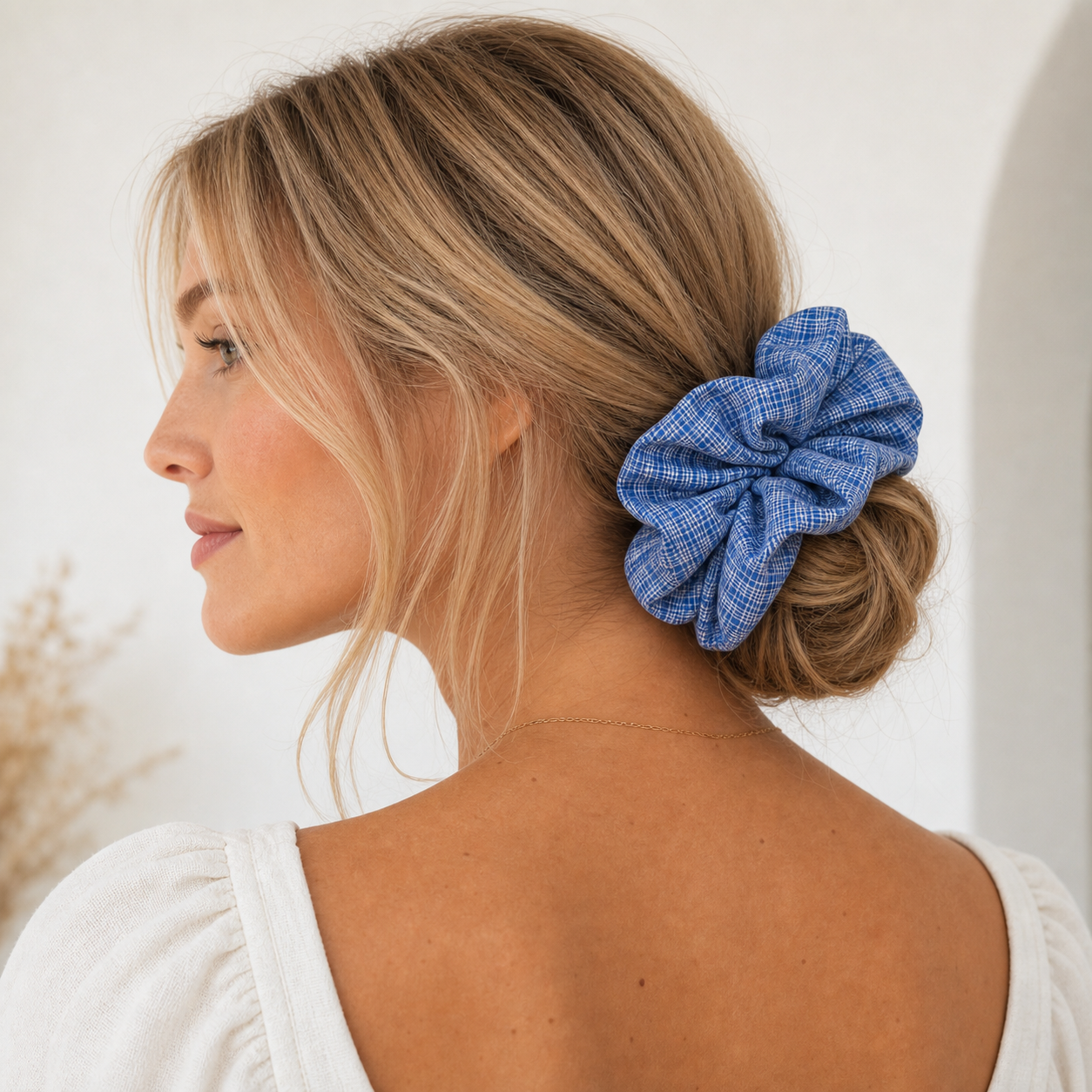 Model wearing a blue gingham scrunchie in a low bun, gentle hold linen hair tie for classic hair care.