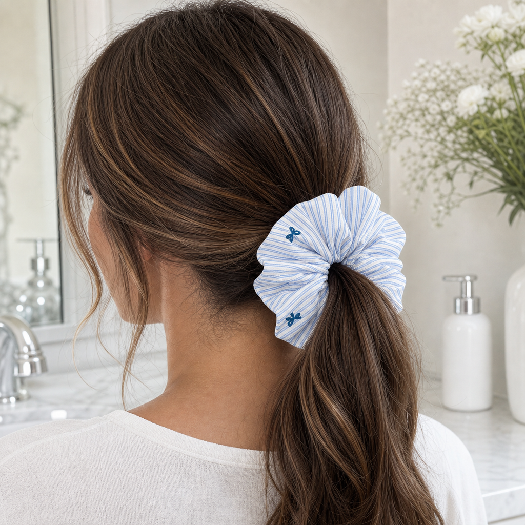 Brown hair model with blue striped bow scrunchie in a low ponytail, preppy style hair protection on linen blend.