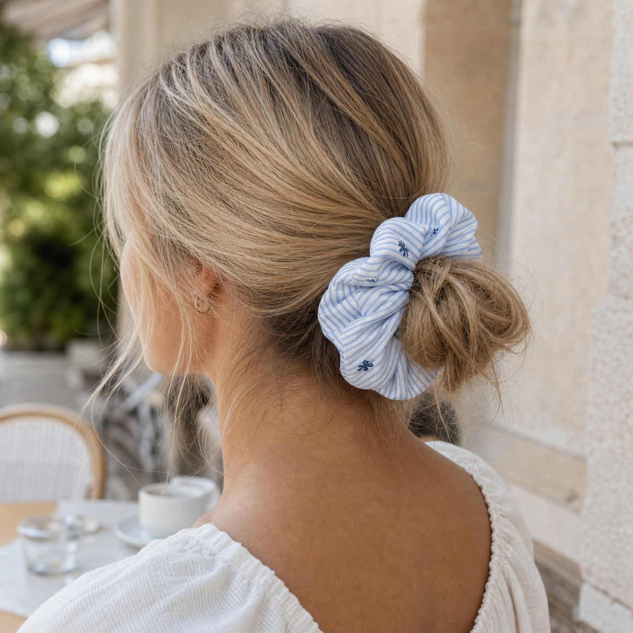 Blonde hair model wearing a blue striped bow scrunchie in a messy bun, classic preppy style hair tie.