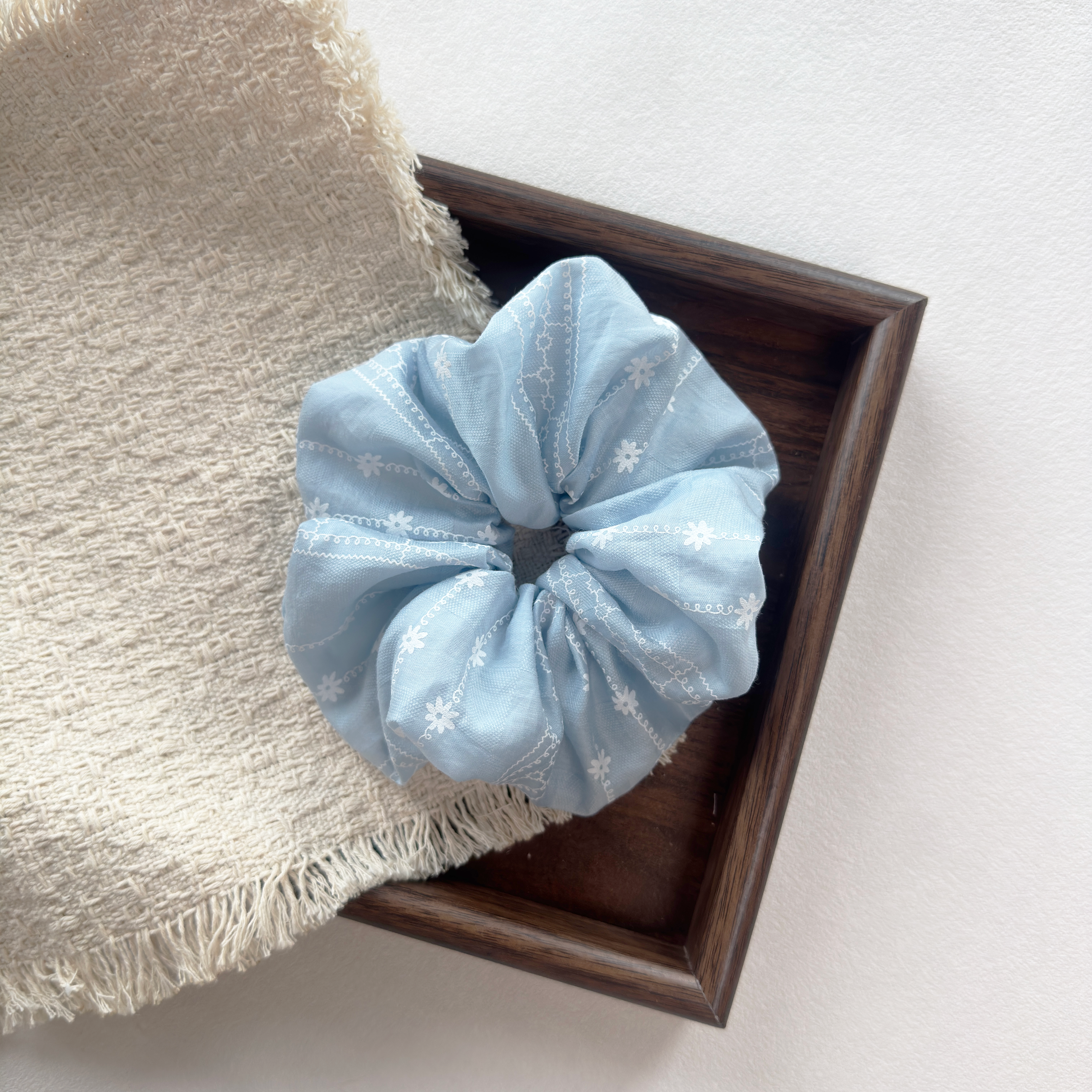 Blue floral scrunchie on a wooden tray, stylish hair accessories for women.