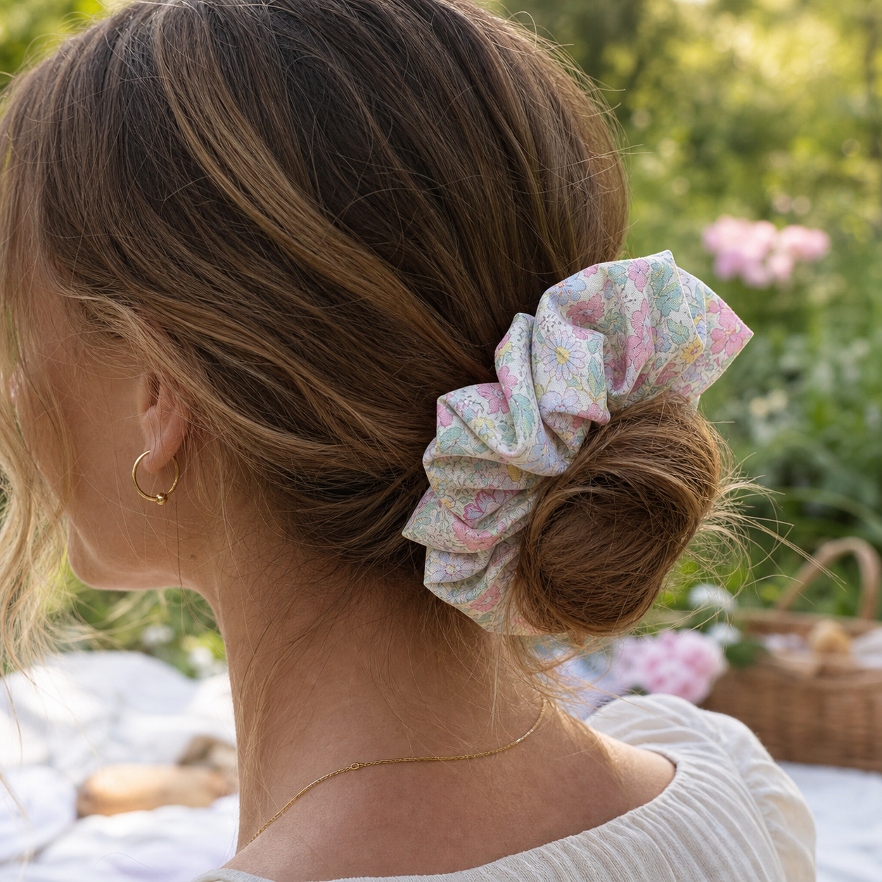 Model wearing a vibrant floral scrunchie in a low bun during a picnic, stylish cottagecore hair protection.