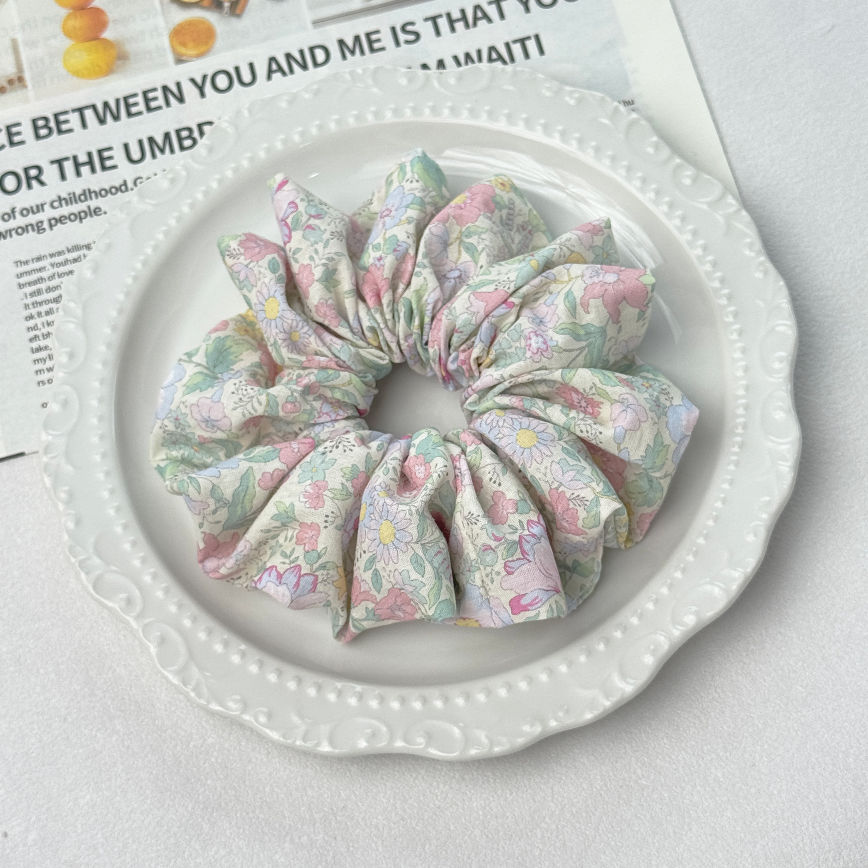 Detailed angle of a dopamine floral scrunchie on a decorative plate, gentle hold for healthy hair care.