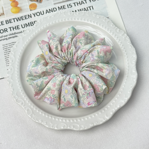 Detailed angle of a dopamine floral scrunchie on a decorative plate, gentle hold for healthy hair care.