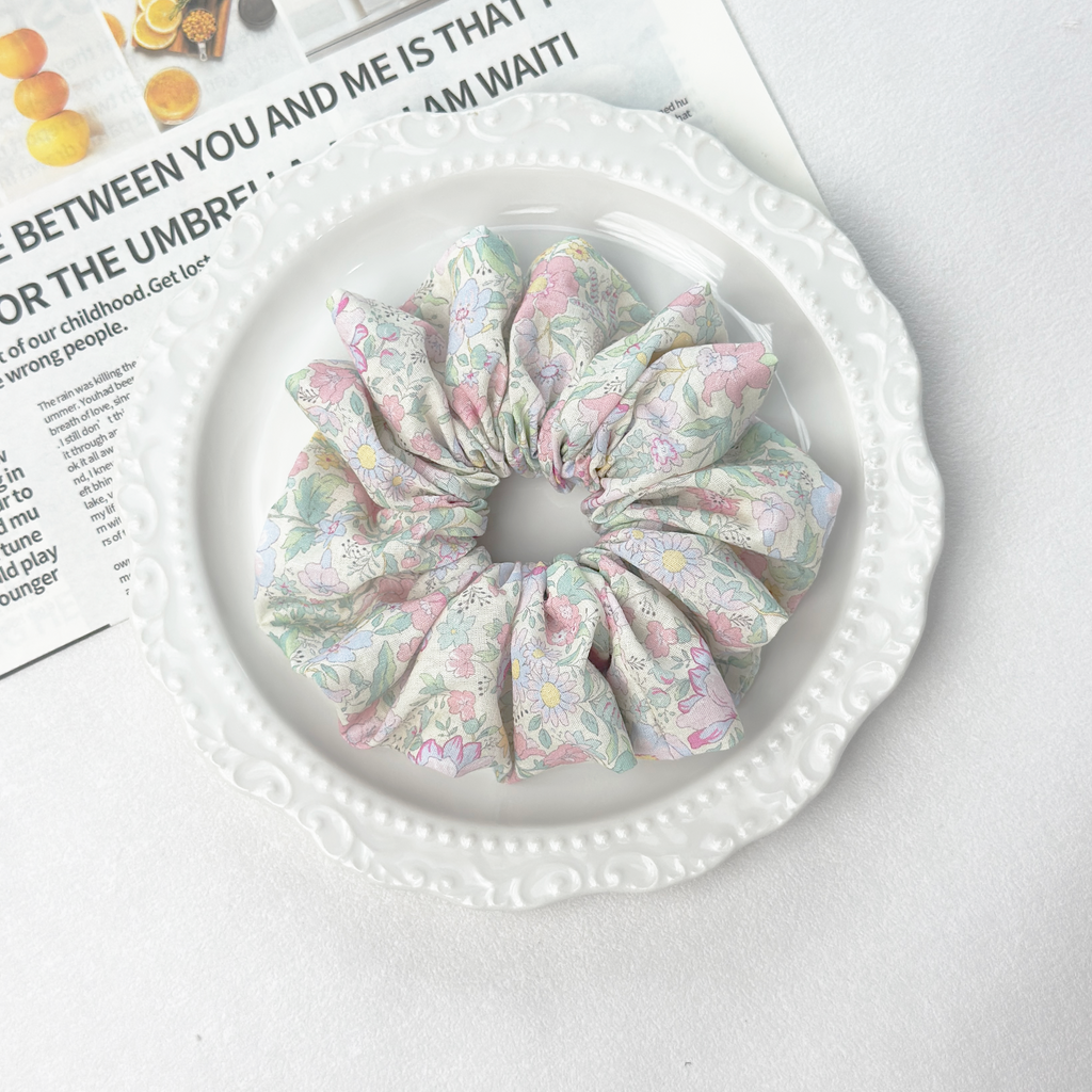 Multi-color floral scrunchie on a white wavy plate with newspaper, vibrant mood-boosting hair tie on linen blend.