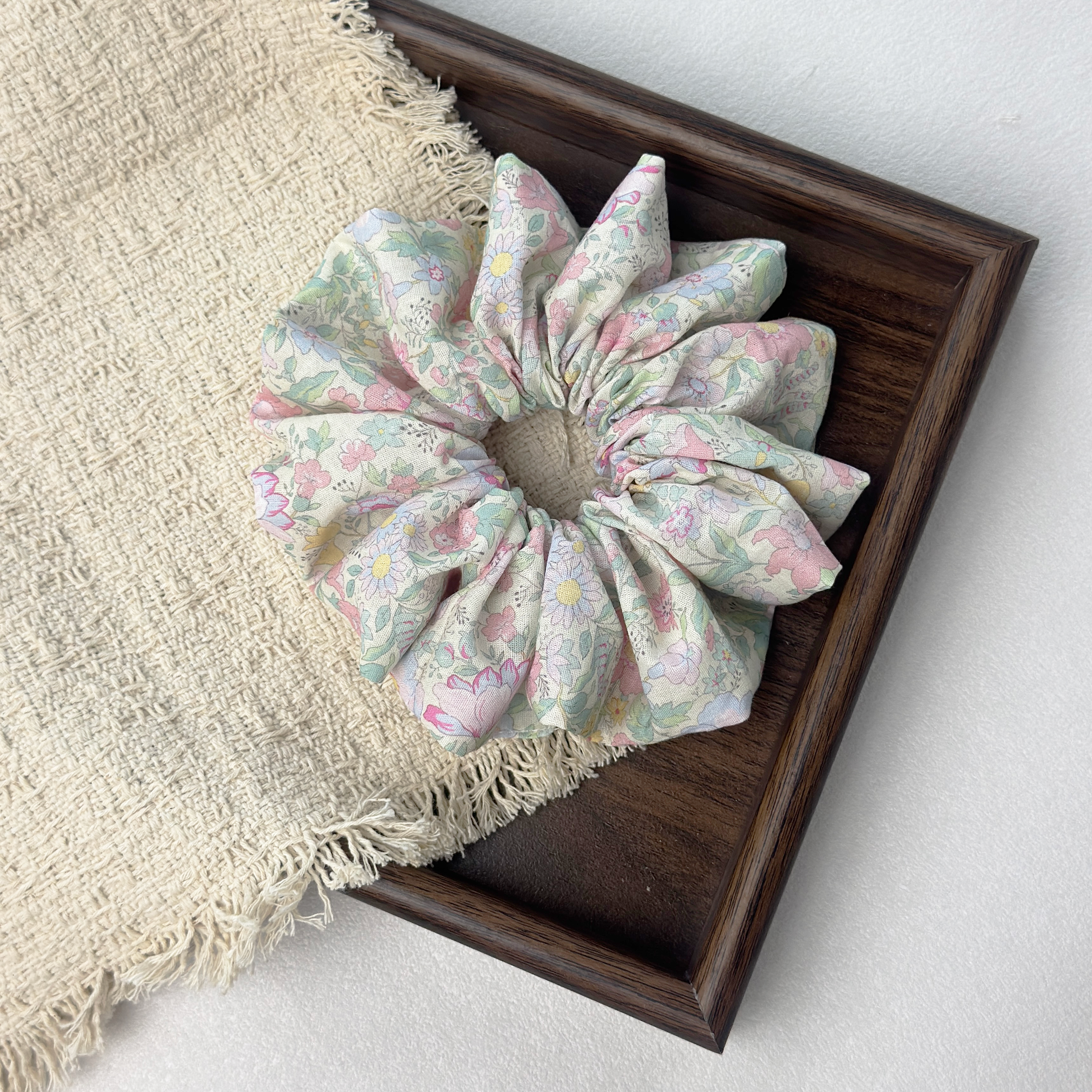 Dopamine floral scrunchie on a wooden tray with beige fringed cloth, premium multi-color linen hair accessory.