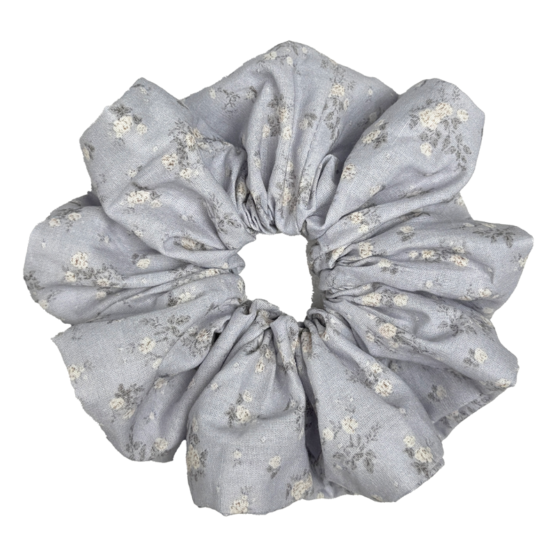 Single dusty blue scrunchie with ditsy white floral print isolated on white background. Voluminous ruffled design with tiny cream blossoms and charcoal-grey stems across a woven cotton base.