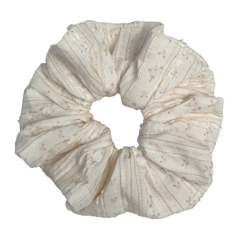 Single cream floral bouquet print scrunchie isolated on white background. Voluminous ruffled design with vertical ribbed texture, dusty pink blossoms, and soft frayed edges.