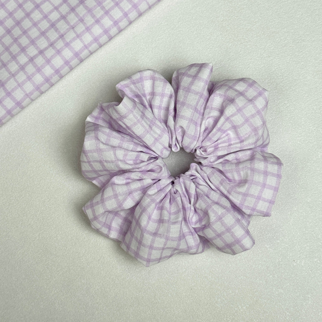 Lavender windowpane plaid scrunchie displayed alongside a matching flat fabric swatch showing the full grid pattern, white pebbled texture surface.