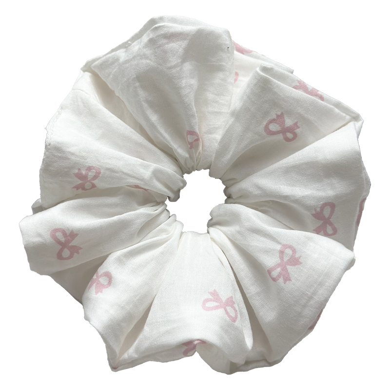 Single white scrunchie with repeating pastel pink bow print isolated on white background. Voluminous ruffled design with soft cotton muslin texture and deep natural folds.
