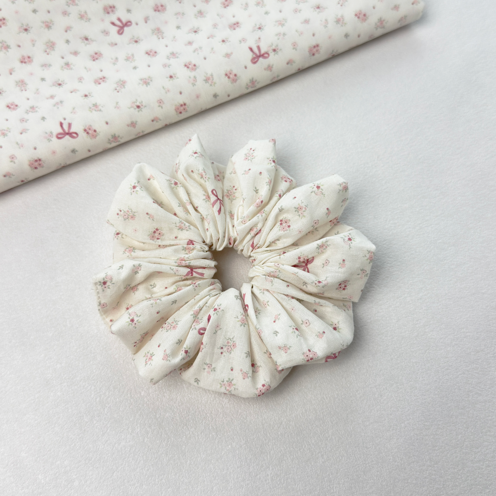 Pink floral bow scrunchie on white background with floral fabric roll, showcasing high-quality material.