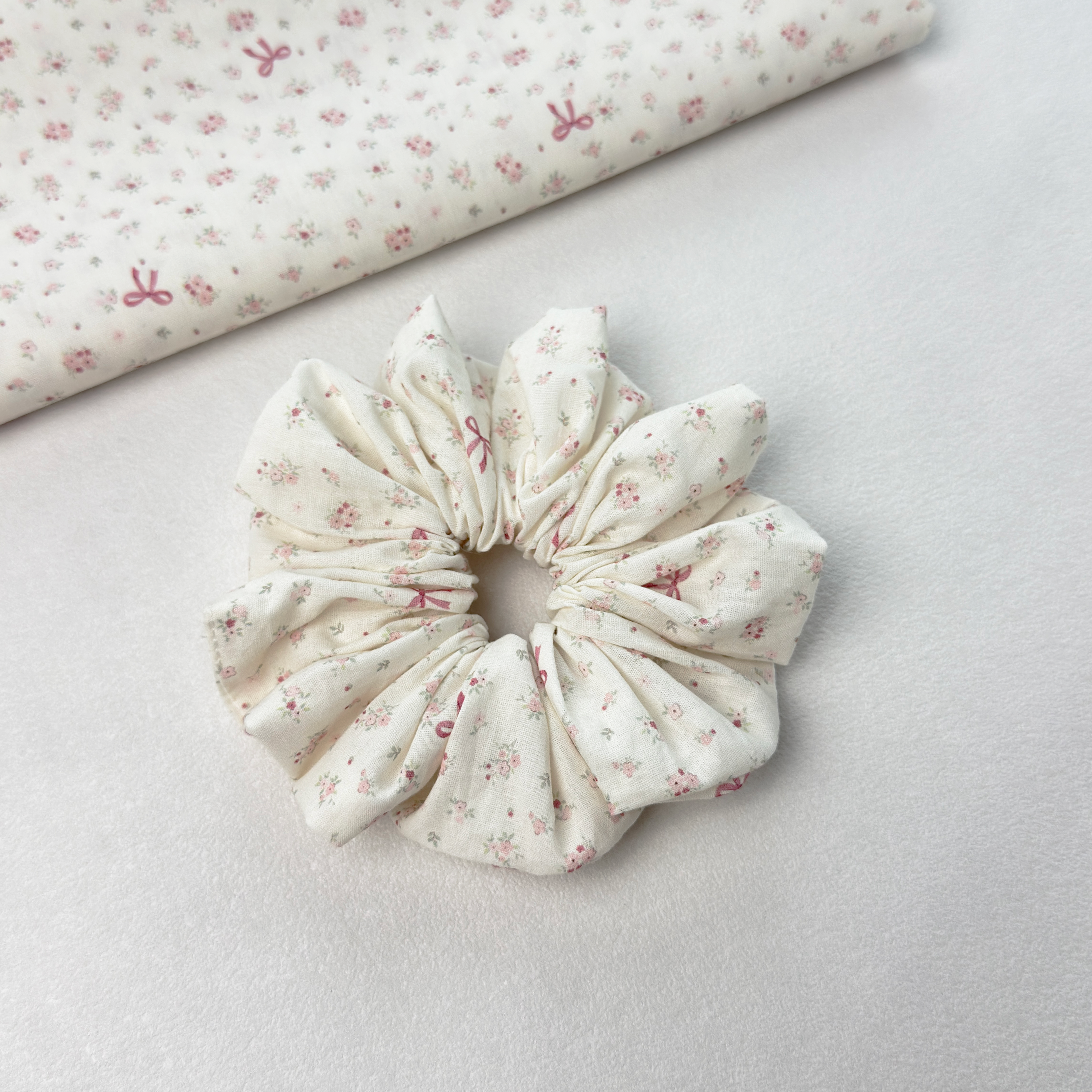 Pink floral bow scrunchie on white background with floral fabric roll, showcasing high-quality material.