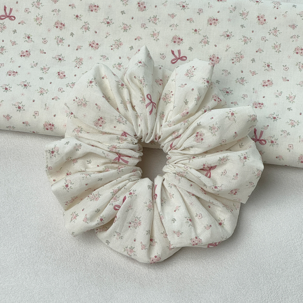 Top-down view of pink floral bow scrunchie with matching fabric swatches, chic vintage floral hair accessory.