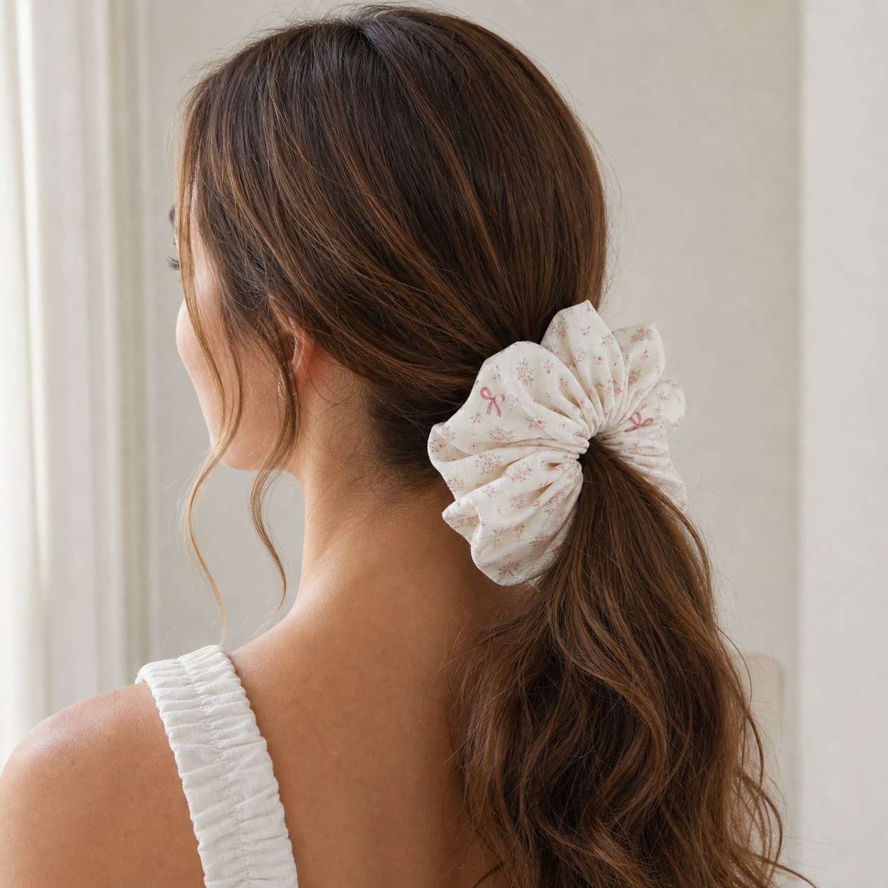 Brown hair model styling a low ponytail with pink floral bow scrunchie, sweet vintage linen blend hair tie.