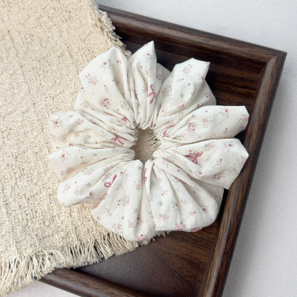 Top view of pink floral bow scrunchie on wooden tray, breathable linen blend material for hair health.