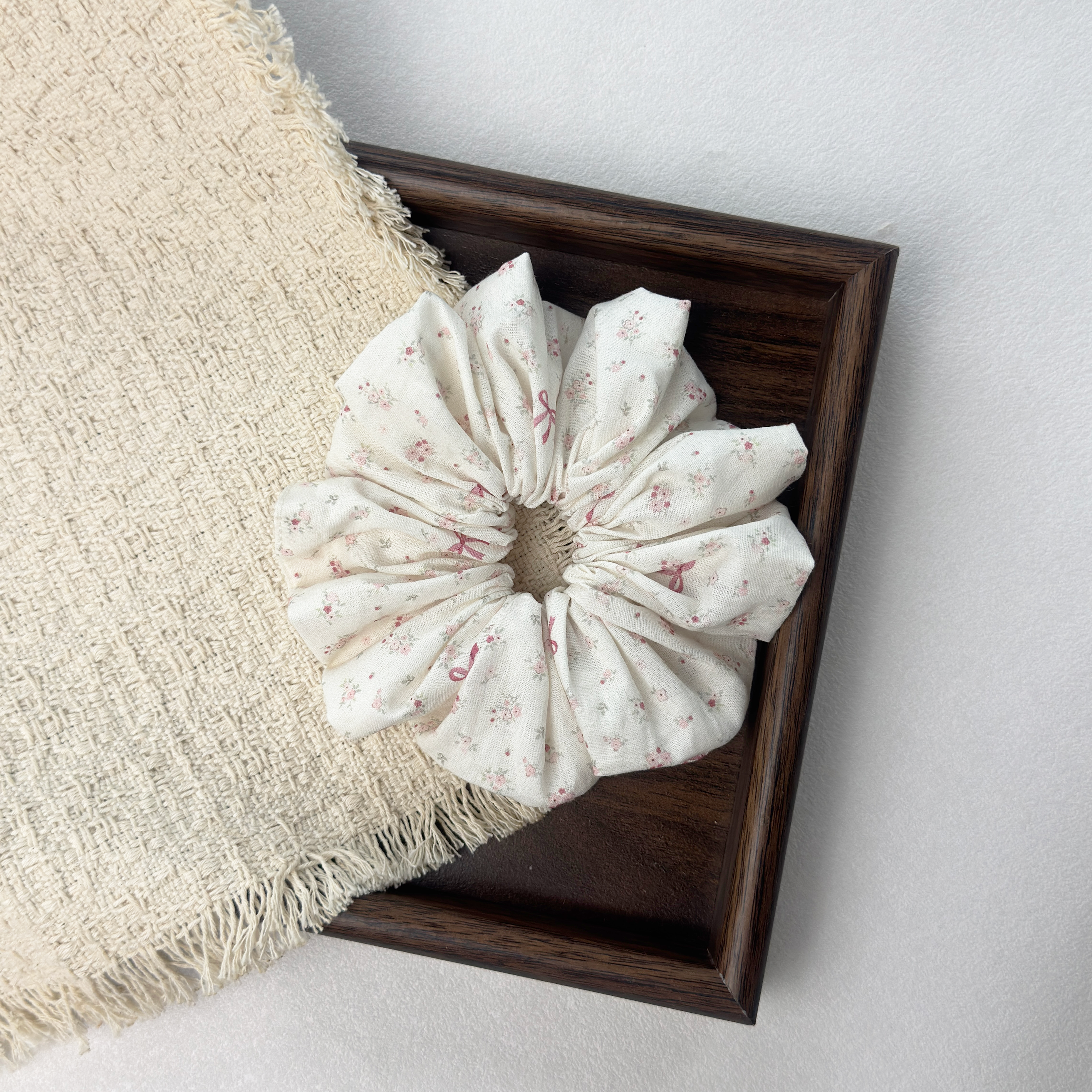 Pink floral bow scrunchie on a wooden tray with beige woven fabric, premium vintage aesthetic hair accessory.