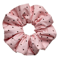 Single baby pink scrunchie with dark brown polka dots isolated on white background. Voluminous ruffled design with soft woven cotton texture and fine edge stitching.