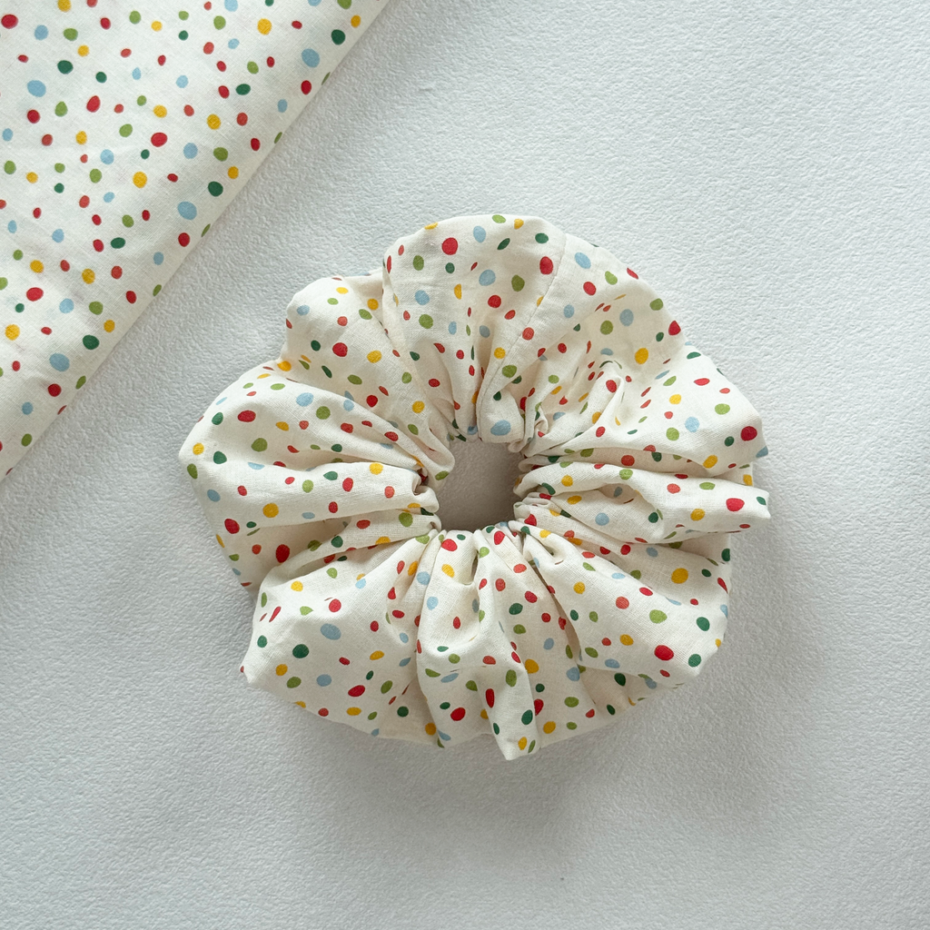Close-up texture of cream linen blend scrunchie with vibrant polka dots.