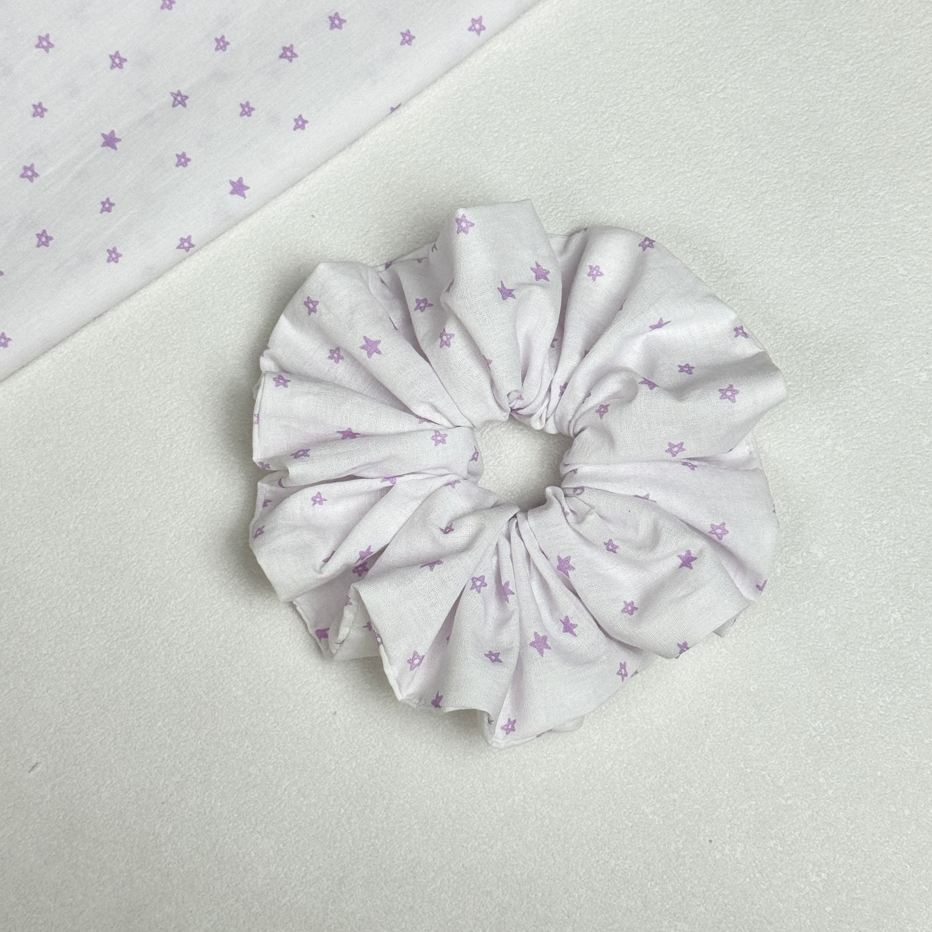 White lavender star print scrunchie displayed alongside a matching flat fabric swatch showing the full star pattern, white pebbled texture surface.