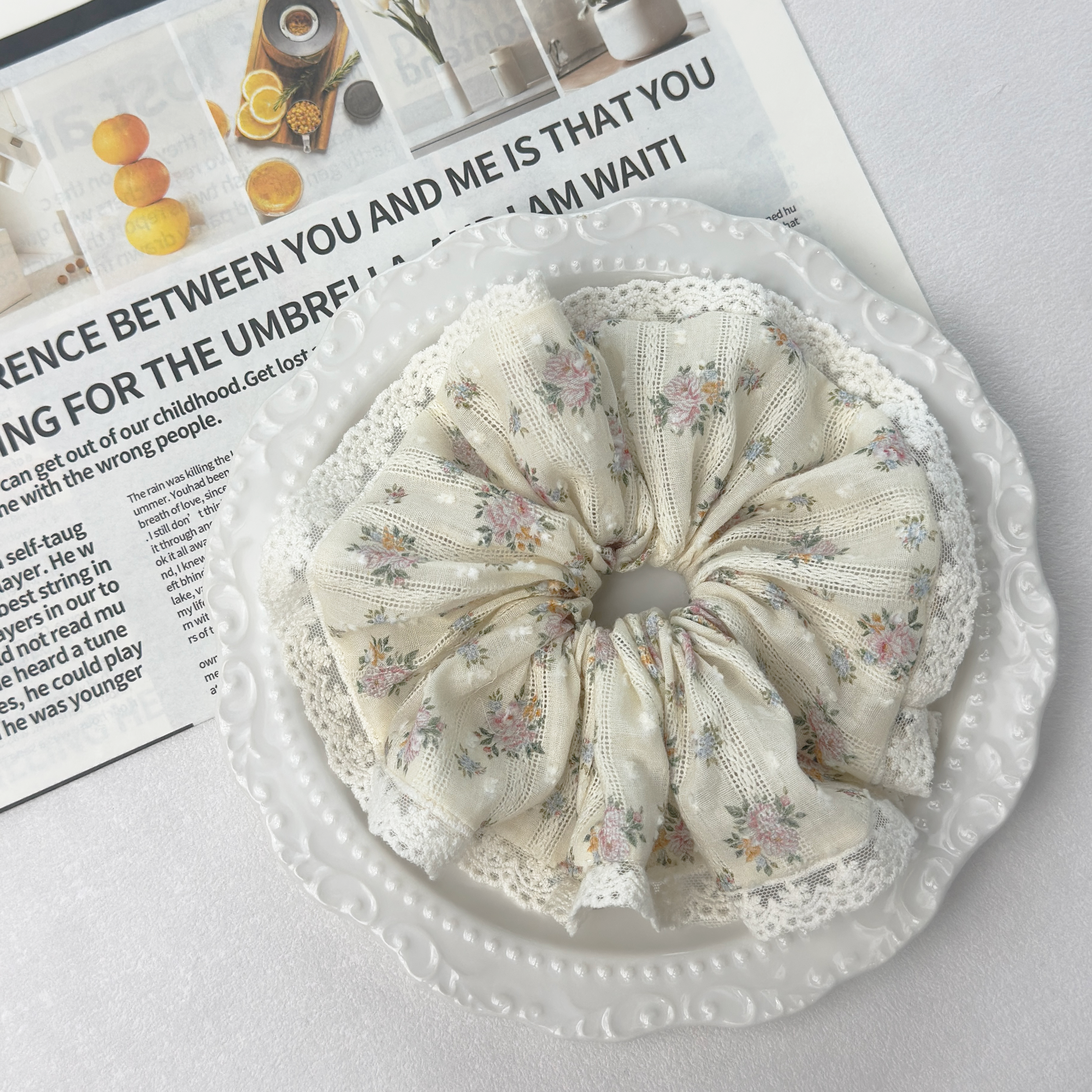 Yellow floral lace scrunchie on a white decorative plate with a newspaper background, romantic cottagecore style.