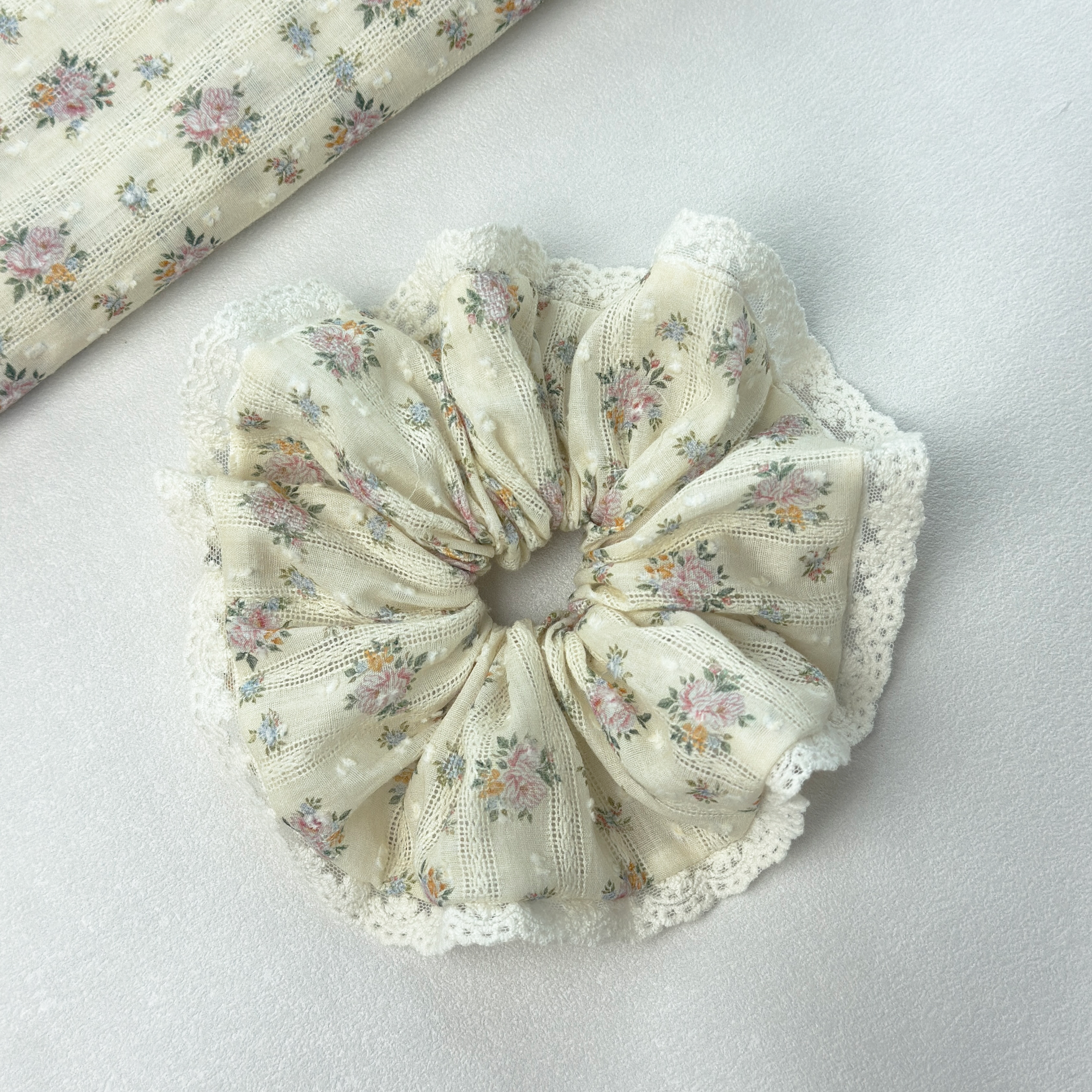 Yellow floral lace scrunchie on white background with a matching fabric roll, premium linen blend hair accessory.