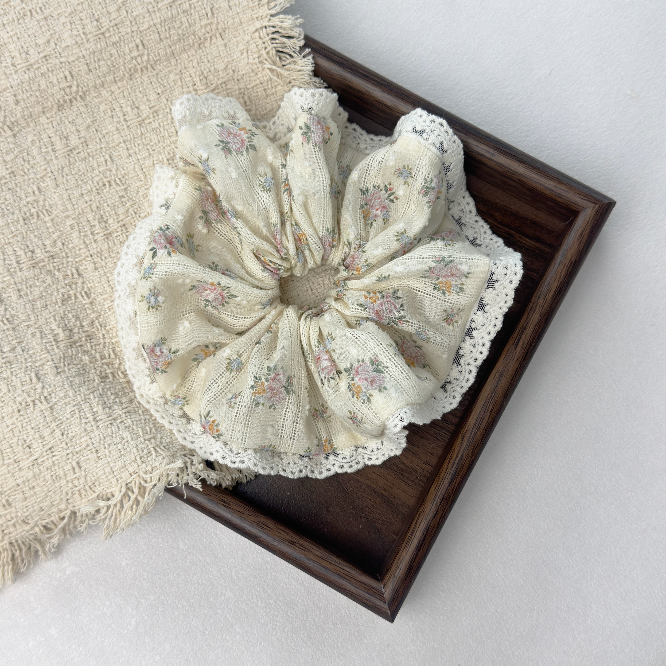 Yellow floral lace scrunchie on a dark wooden tray with a beige woven mat, chic vintage aesthetic.