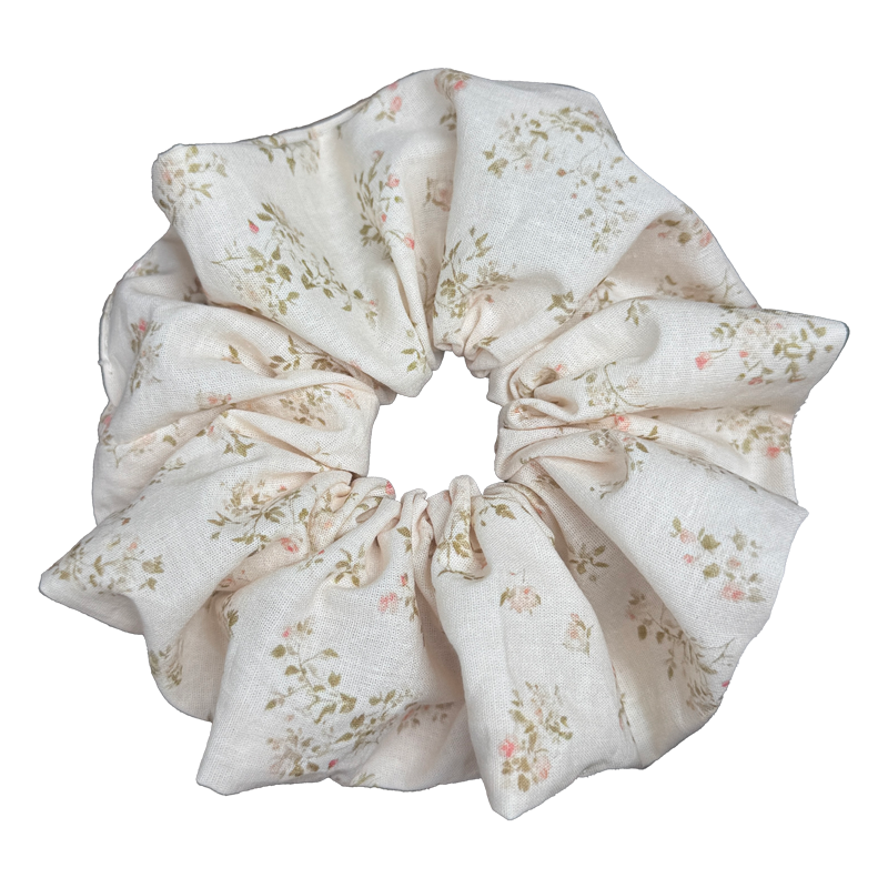 Single cream yellow floral print scrunchie isolated on white background. Voluminous ruffled design with pale pink blossoms and olive green leaves on a soft cream base.